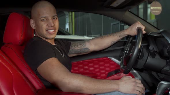 Happy Handsome African Man Smiling to the Camera Sitting in His Sports Car alt