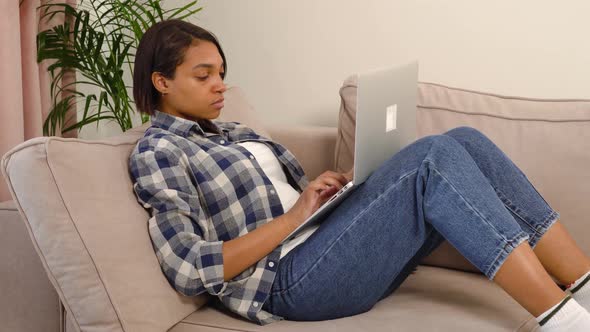 A Tired Young AfricanAmerican Woman is Typing Text at Home on a Laptop