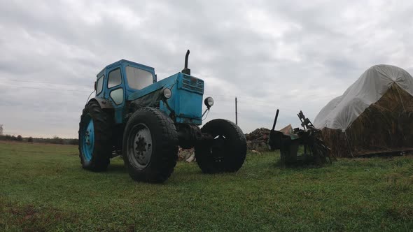 Grey Rainy Clouds Over a Vintage Blue Tractor in the Countryside. Unprofitable Agribusiness alt