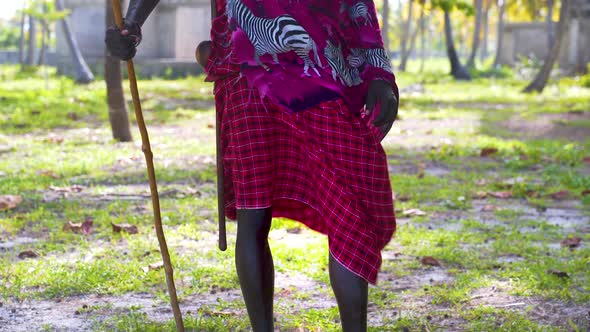 Native african man in pink traditional clothing, holding wooden stick. alt