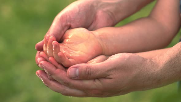 Father Holding Hands Of His Child And Water Drops Falling In Their Palms In Slow Motion alt