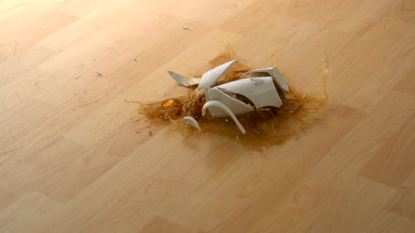 Drpping cup of coffee and breaking on wooden floor, Slow Motion alt