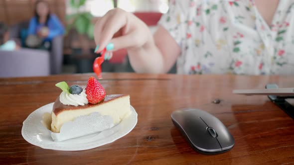 Hand freelancer Asian woman scooping the delicious cake and using laptop in coffee shop