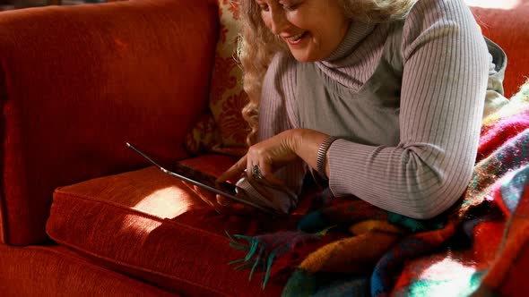 Mature woman using digital tablet in living room 4k alt