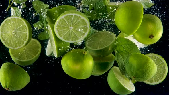 Limes with mint leaves splashing into the water in slow motion. Lots of limes perfect for mojito