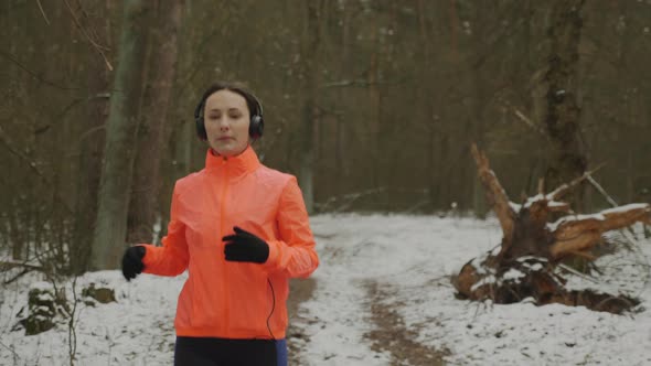 Woman jogging in winter park wearing orange sportswear training for marathon. Running concept alt