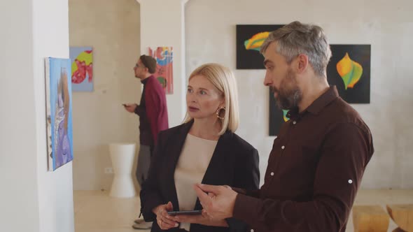 Man and Woman Discussing Abstract Painting in Gallery alt