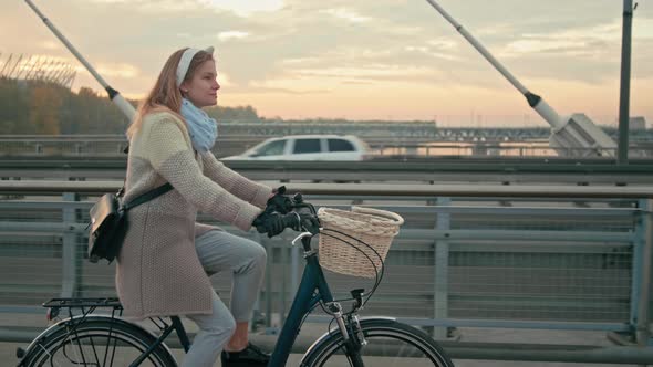 Woman Is Going To Work By Bicycle in City on Suspension Bridge in Autumn