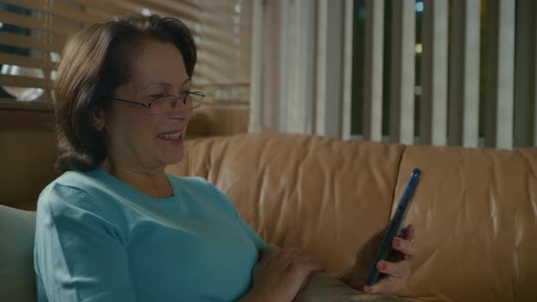 Elderly Woman with Glasses and Dark Hair Talking Excitedly on Smartphone