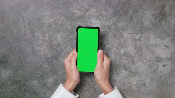 Top view, Woman hands using smartphone with mock-up chroma key green screen display on desk.