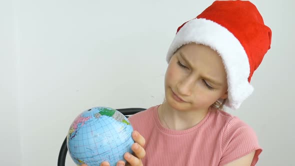 Earth Globe with Geographical Names in Ukrainian Cyrillic Letters is Held By Blond Girl in Santa Hat alt