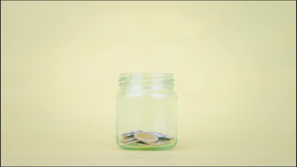 Stop motion animation coin into a clear glass jar on yellow background