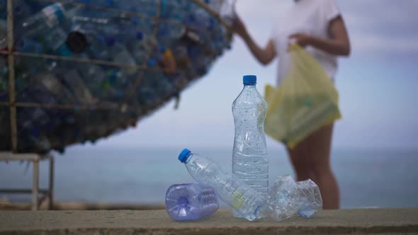 Used Empty Water Bottles with Unrecognizable Blurred Young Woman Passing at Background Putting Waste alt