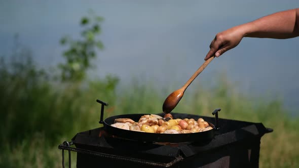 Frying pan from disc harrow with a lid for cooking over an open fire. the cook uses a wooden spoon
