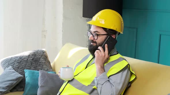 Architect Talking on the Phone and Drinking a Cup of Tea Relaxing on Sofa alt