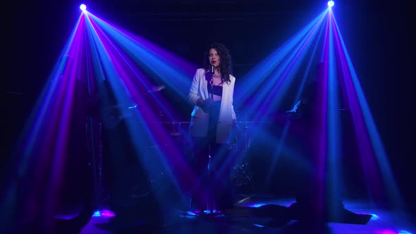 A Stylish Girl Vocalist Sings on Stage in a Vintage Microphone. In the Background Musicians alt