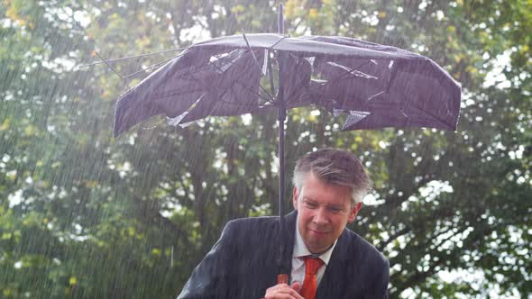 Businessman Sheltering Underneath a Broken Umbrella in the Rain