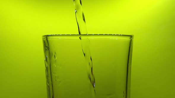 Close up shot of plastic bottle pouring water in glass. Green background. Static alt