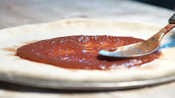 A close-up of a pizza dough on a steel tray on wooden counter while an expereinced chef put juicy re alt