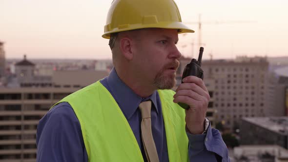 Construction manager on rooftop talking on walkie talkie