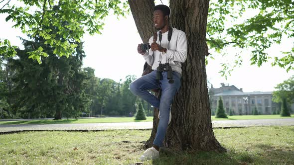 Wide Shot Happy Talented African American Photographer Standing at Tree Leaning on Trunk Watching alt