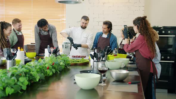 Multi-ethnic Group of Cooking Class Students Watching Cook Making Meal alt