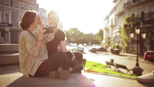 Young Beautiful Couple Taking Pictures Smiling Speaking Sitting in City Park alt