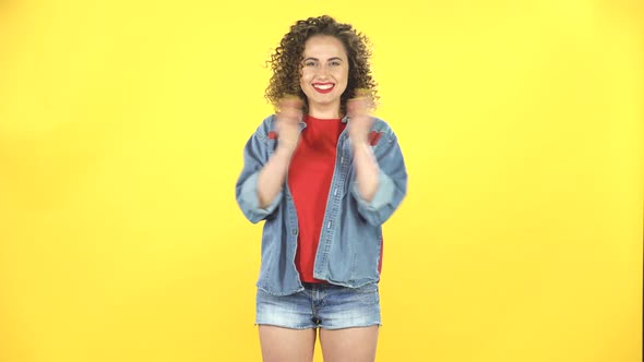 Girl Claps Her Hands with Joy and Delight, Then Shows the Sign Like on Yellow Background at Studio alt