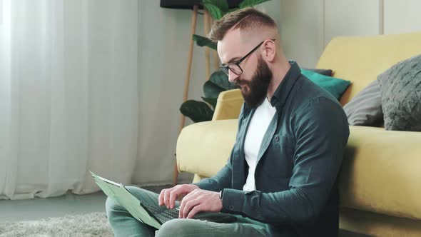 Man Working at the Computer with a Lot of Reminder Notes Sitting Near Sofa alt