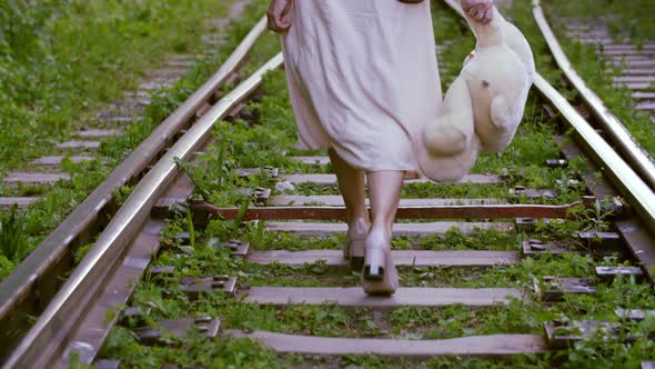 Female Feet in Shoes High Heels Walking on Railway with Teddy Bear in Hand. Woman Stepping in Sexy alt