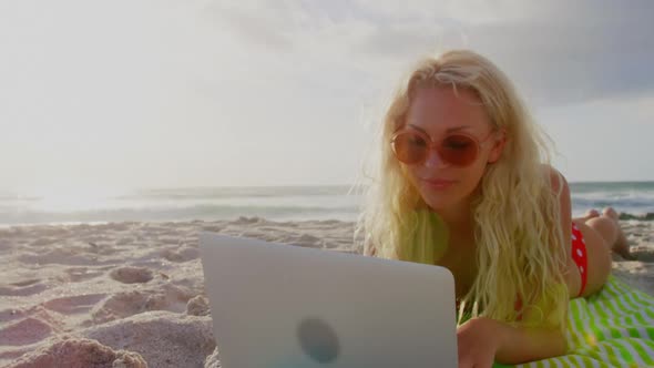 Woman in bikini and sunglasses using laptop on beach 4k
