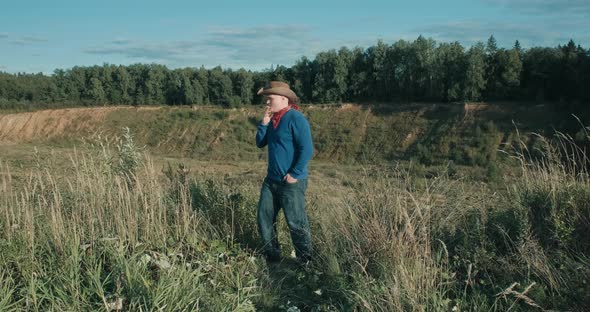 Man in Cowboy Hat Stand on Edge of Sandy Ravine Overgrown with Forest