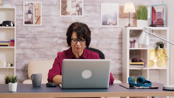 Elderly Age Woman Taking a Sip of Coffee While Browsing on Laptop alt