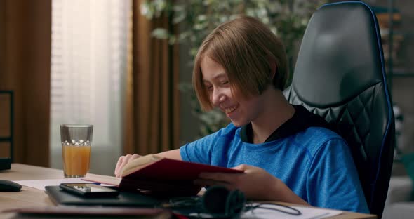 An Ambitious Teenager Sits in Room in the Morning Holds a Book a Notebook in Hands alt
