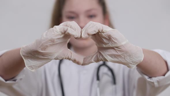 Closeup Little Female Hands in Medical Gloves Showing Heart Shape with Blurred Smiling Pretty Kid alt