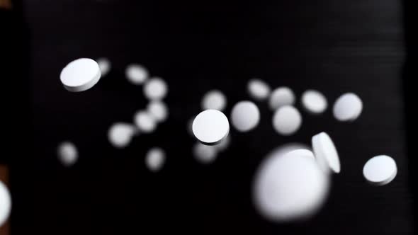 Round white pills on a black background. Super slow motion. Macro alt