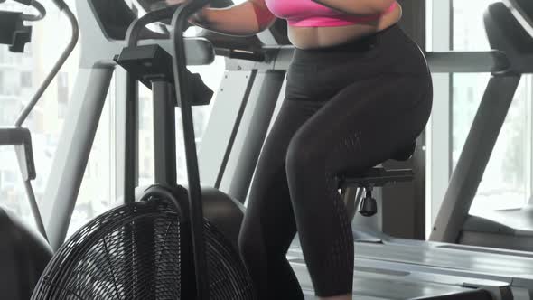 Beautiful Curvy Woman Smiling To the Camera Doing Cardio on Air Bike at Gym alt