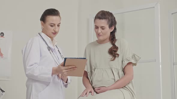 Doctor and Pregnant Woman Looking at Tablet and Talking alt