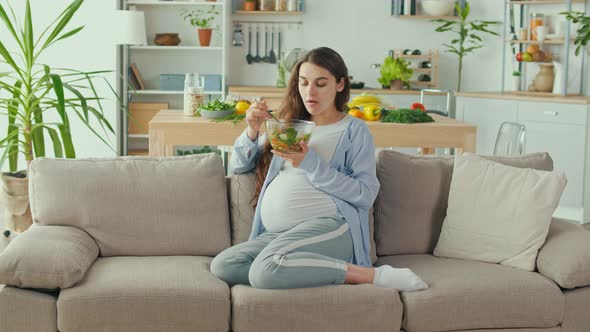 Pregnant Woman With Great Pleasure Eating Vegetable Salad on the Couch alt