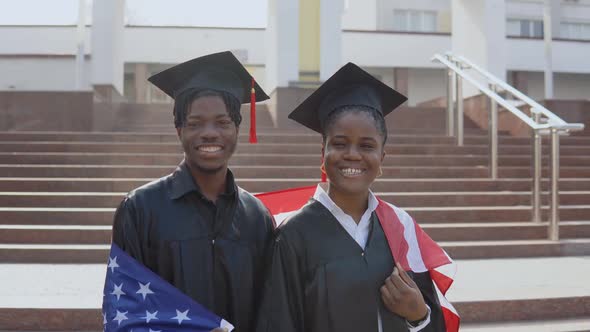 African American Man and Woman Stand Side By Side Facing the Camera in Black Robes and Square Hats alt