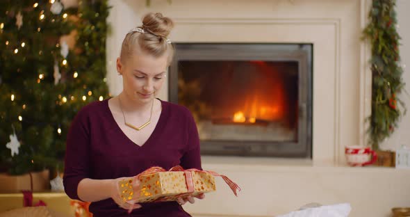 Young Woman Holding Christmas Present Against Fireplace alt