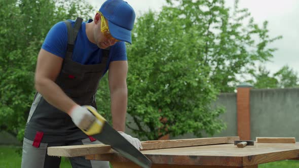 Male Carpenter with a Saw with Protective Tools Sawing Hand Saw Wood alt