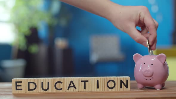 Hand Puts Money in Piggy Bank Next to Which There are Cubes with Inscription Education alt