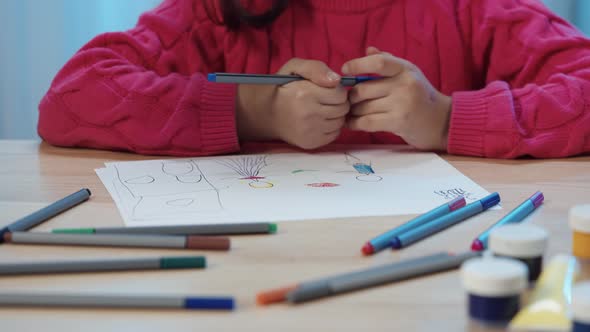 Little Schoolgirl Sitting at the Table in the Room and Drawing with Felttip Pens in the Album alt