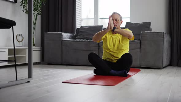 Serious Young Man Meditating at Home Moving Hands in Namaste on Yoga Mat alt