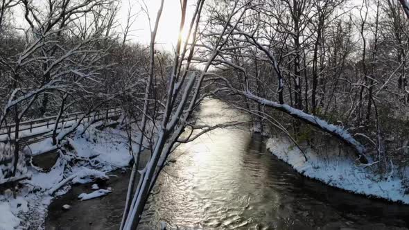 Rising aerial shot over wintry creek and forest in Michigan, USA alt