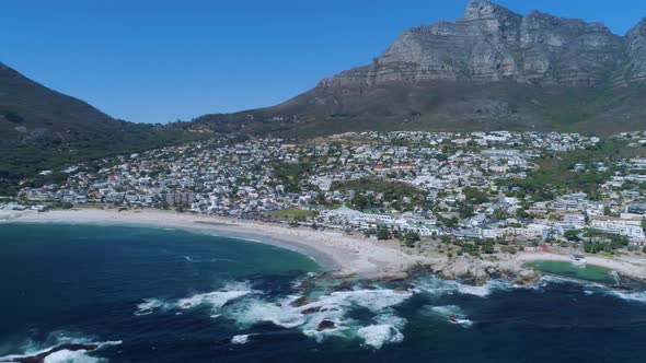 Drone flying backwards, revealing popular Camp's Bay beach and Table Mountain in background alt