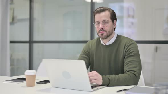 Young Businessman Looking at Camera While Using Laptop in Office alt