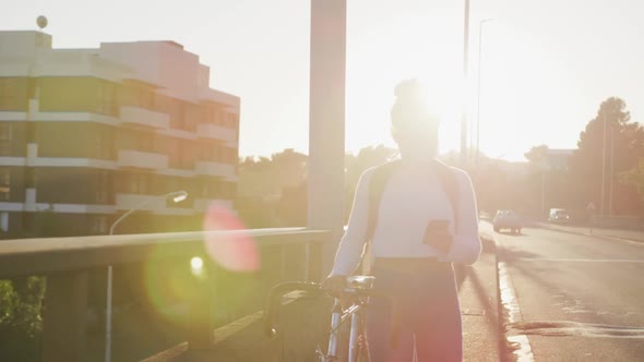 Mixed race woman walking next to her bike on the street alt