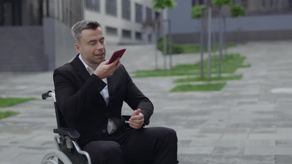 Crop View of Positive Disabled Man in Formal Suit Dictating Voice Message and Sending Outdoors alt
